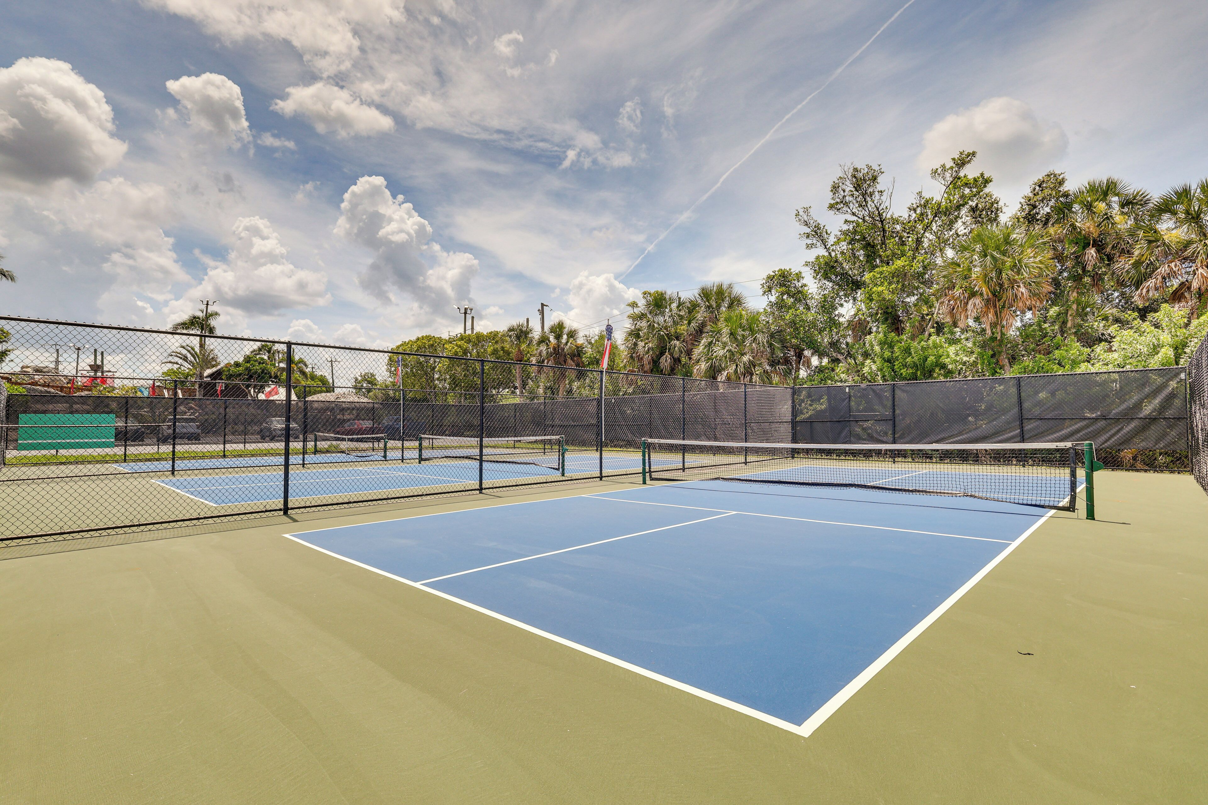 Un court de tennis avec un filet, entouré d’une clôture et d’arbres.