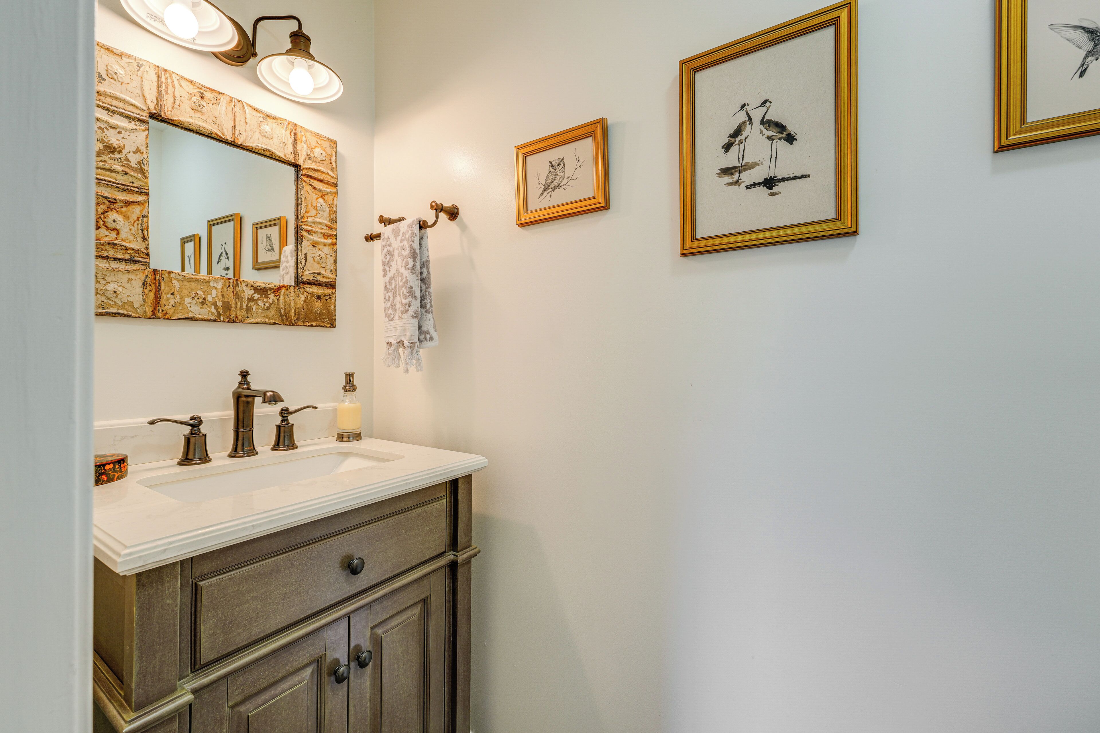 Une salle de bain avec un lavabo en marbre, un grand miroir et des œuvres d’art encadrées accrochées au mur.