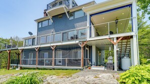 Ein modernes Haus mit zwei Etagen, einem großen Balkon, einer überdachten Veranda und einem sichtbaren Wassertank.