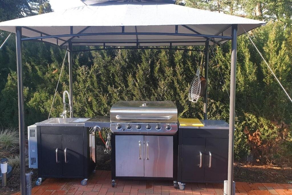 An outdoor grill setup with a canopy, a sink, and storage cabinets.