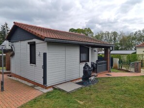 A single-story house with a tiled roof, a small porch, and a front yard with a sculpture.