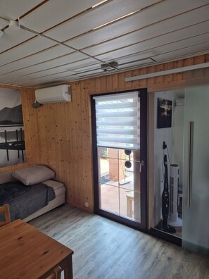 A compact room with a sofa, a table, and a sliding glass door leading to an outdoor area.