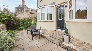 Una casa con fachada de piedra, puerta principal negra y un pequeño patio con mobiliario exterior.
