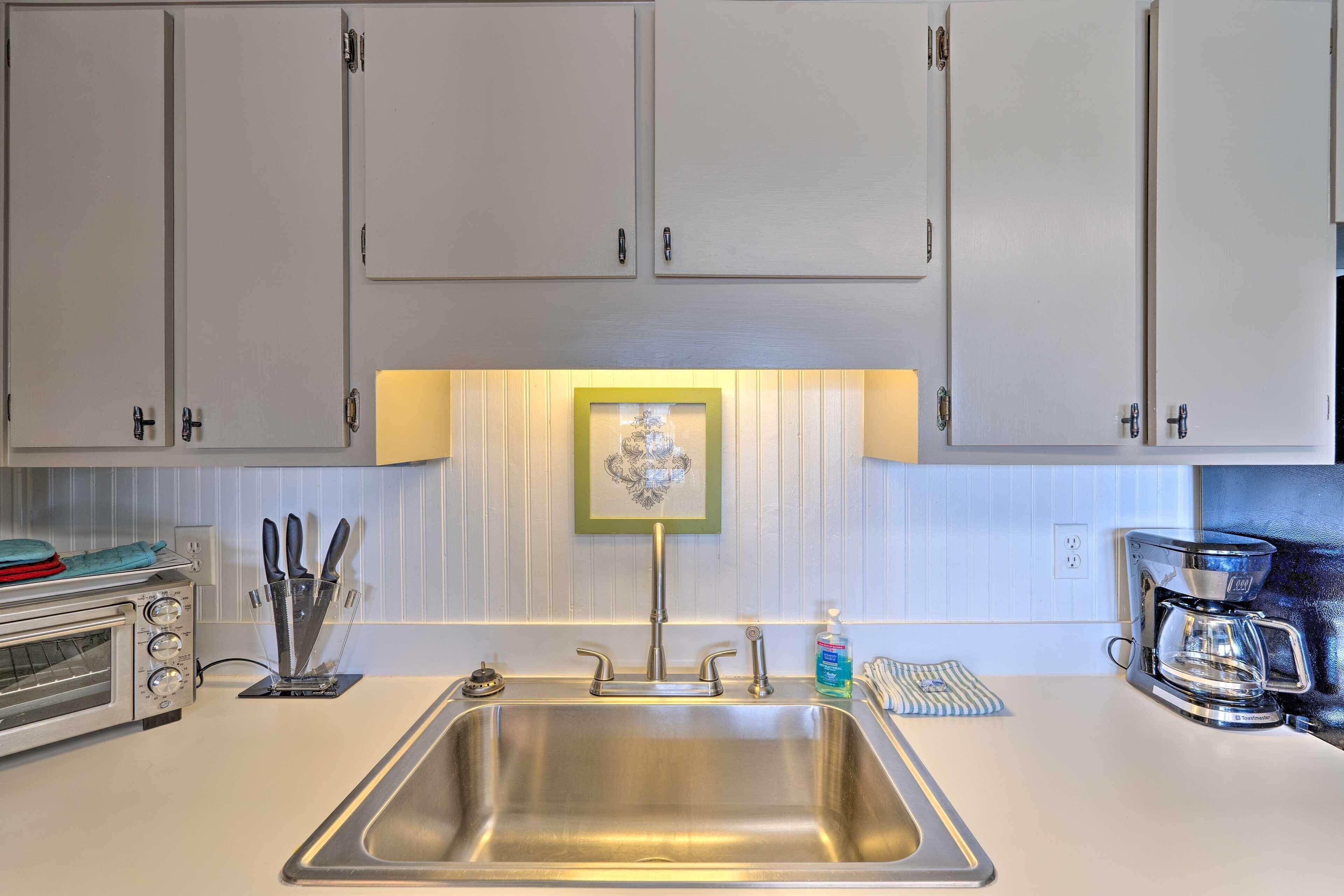 A kitchen with a stainless steel sink, a toaster oven, a coffee maker, and a framed picture above the sink.