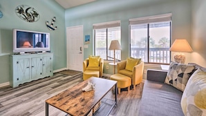 A living room with a TV, two yellow armchairs, a sofa, a wooden coffee table, and a ceiling fan.
