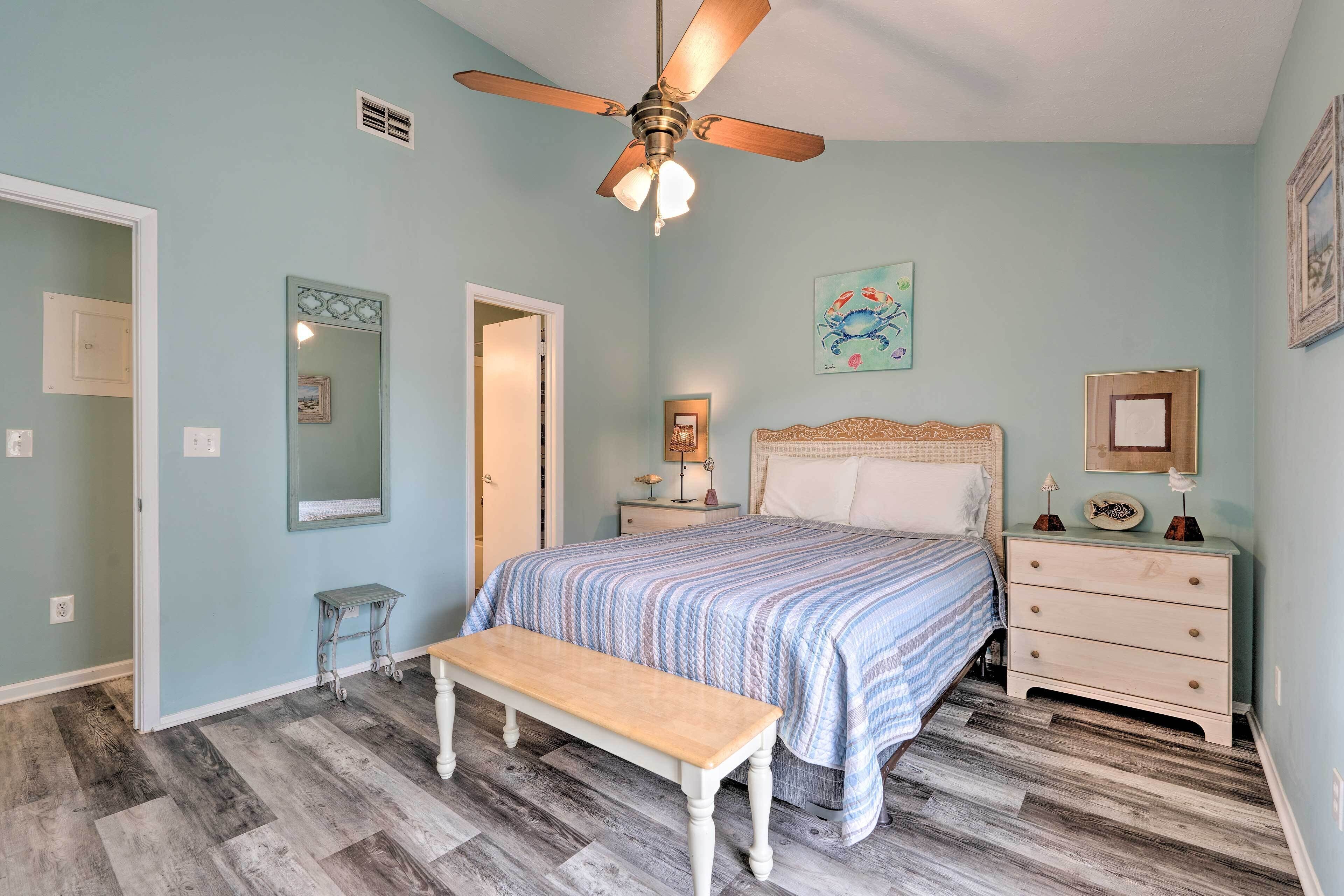 A bedroom with a bed, a bench, a nightstand, a mirror, and a ceiling fan.