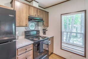 A modern kitchen with wooden cabinets, a black refrigerator, a stove, and a window with blinds.