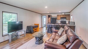 Ein modernes Wohnzimmer mit einer Ledersofa, einem Glastisch und einem Flachbildfernseher. Es gibt einen Essbereich mit Tisch und Stühlen sowie eine Küche mit Holzausbau und Geräten.