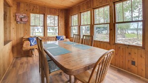 Una cabaña de madera con comedor que incluye una mesa grande y sillas, un banco con cojín y vistas al exterior.