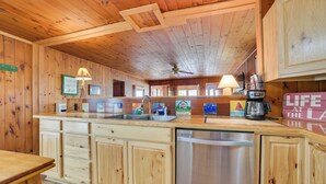 Una cocina de estilo cabaña de madera con una isla central, electrodomésticos de acero inoxidable y un ventilador de techo.