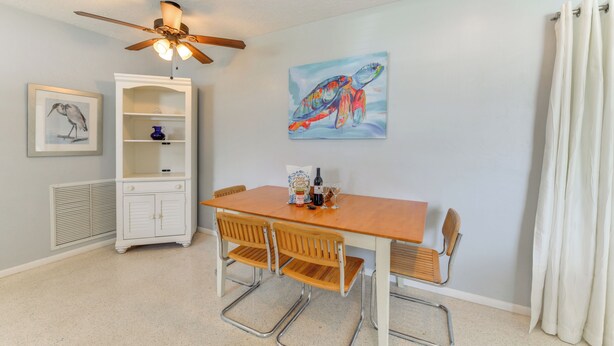 A dining area with a wooden table and metal chairs, a ceiling fan, a white cabinet, and a painting of a turtle on the wall.