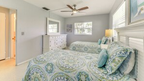 A bedroom with two beds, a ceiling fan, a dresser, and a window with blinds.