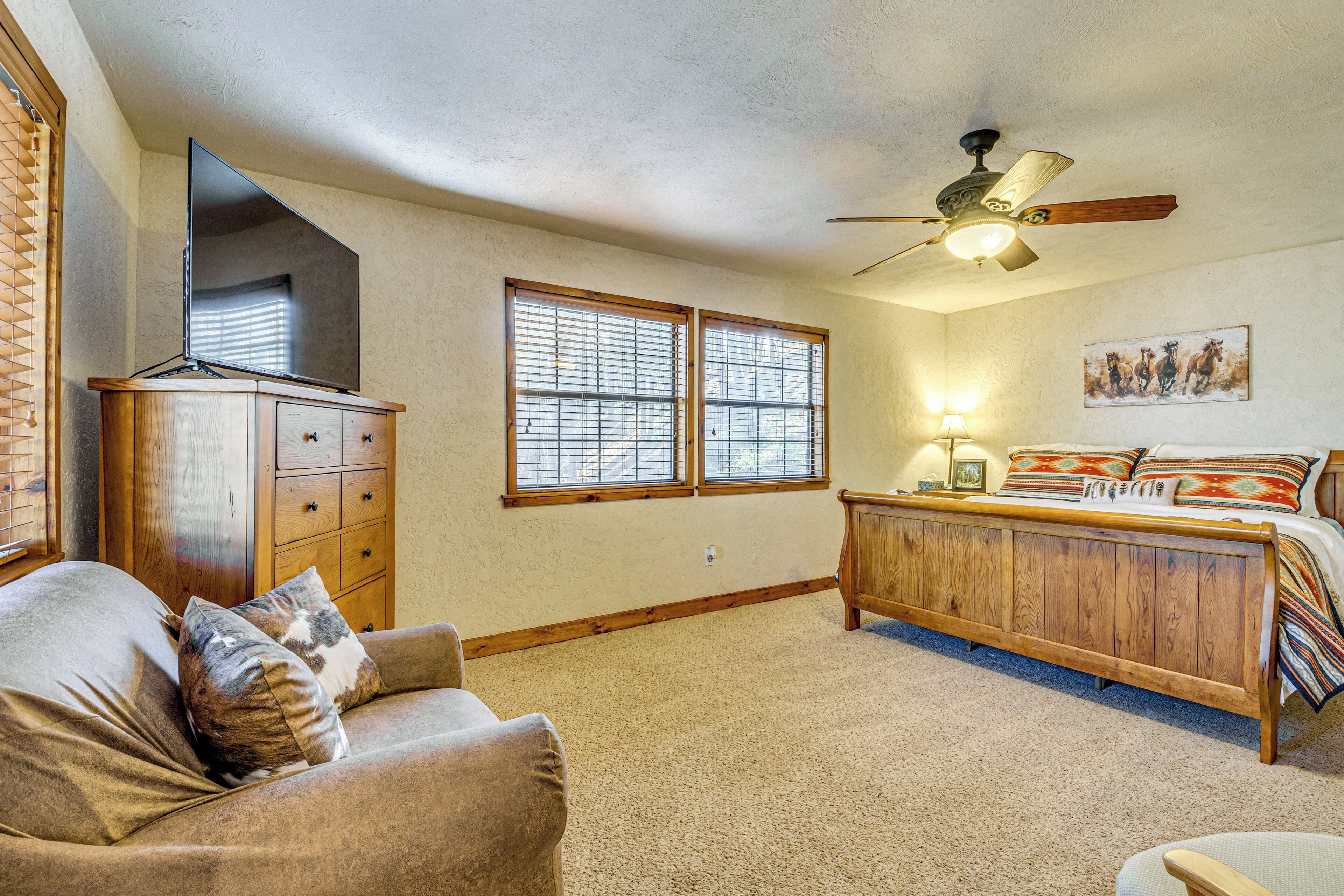 A bedroom with a bed, a wooden dresser, a ceiling fan, and two windows with blinds.