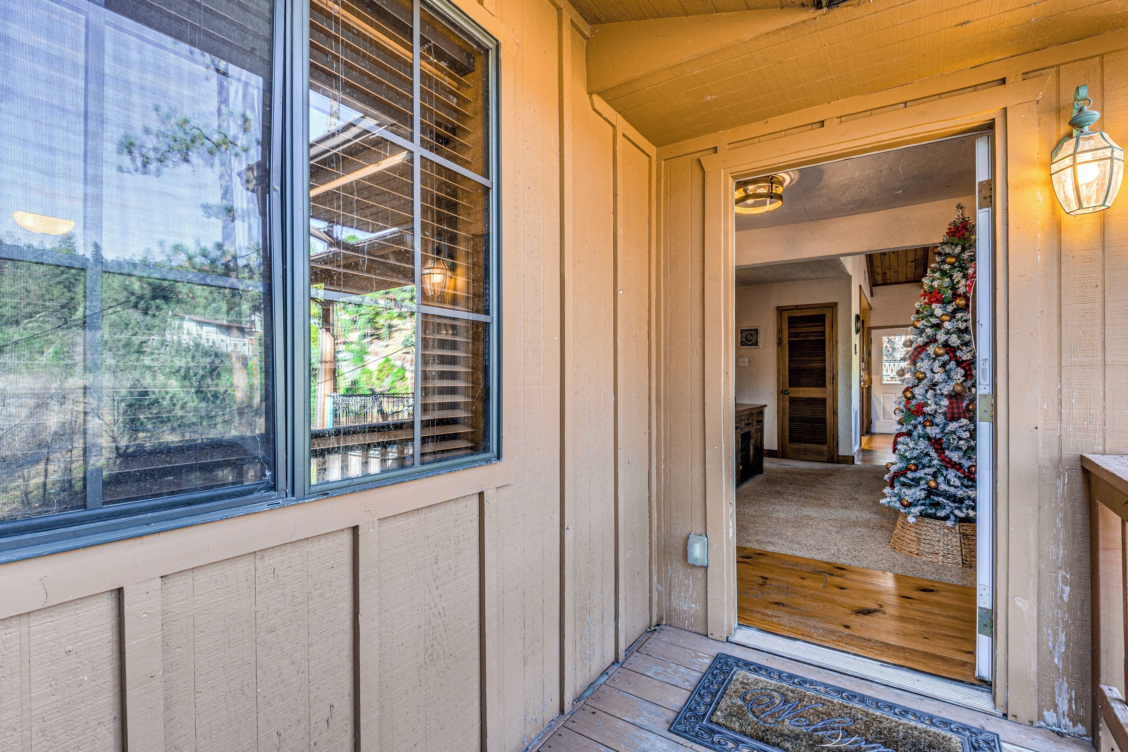 A wooden exterior with a large window and a door leading to an interior with a Christmas tree.