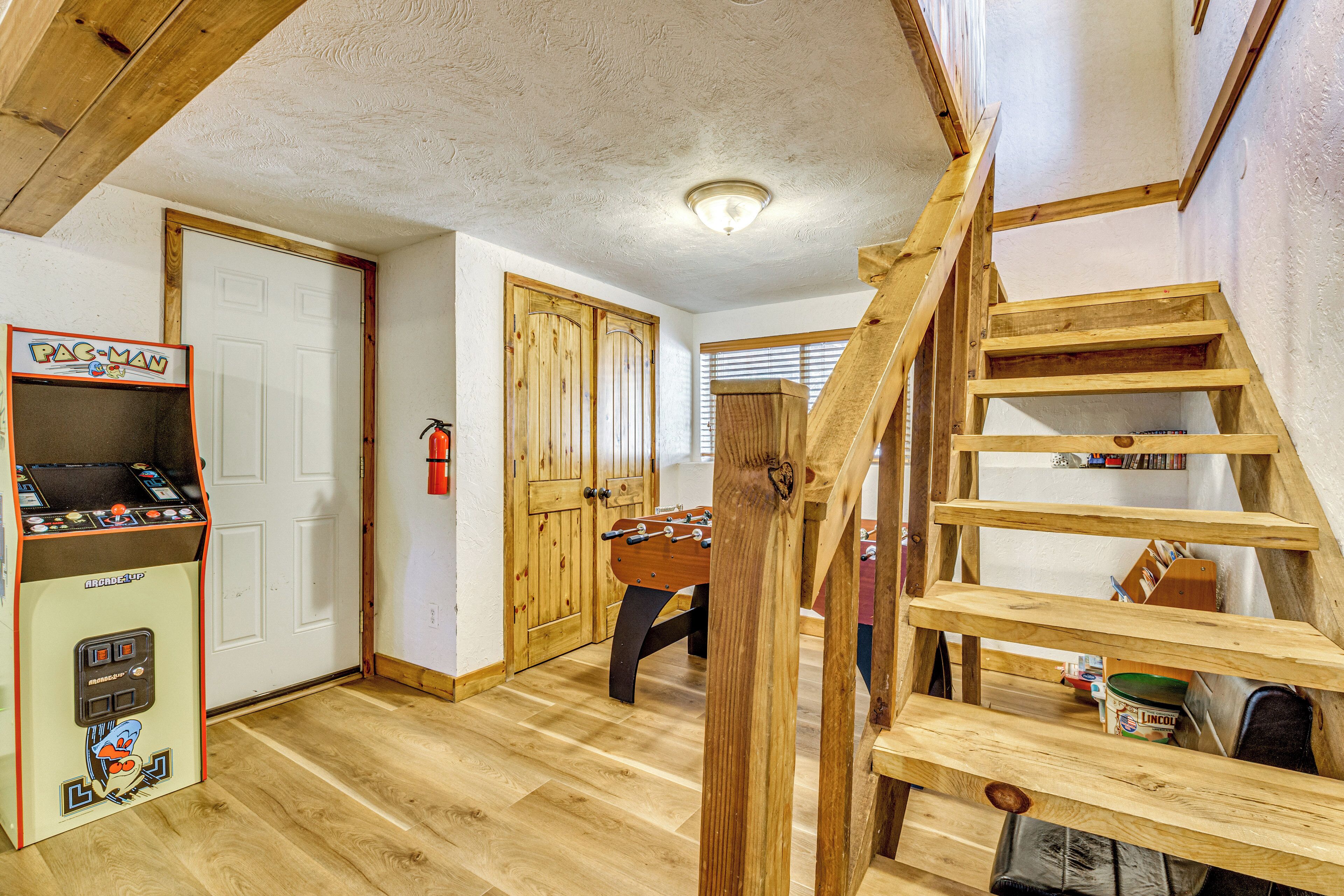 A room with a wooden staircase, a foosball table, and a Pac-Man arcade machine.