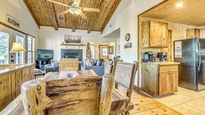 A spacious living area with a wooden dining table and chairs, a fireplace, and a kitchen with wooden cabinets and a stainless steel refrigerator. - Hot Tub Haven w/ Game Room & Grill in Ruidoso! (Ruidoso)