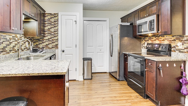 A kitchen with wooden cabinets, a stainless steel refrigerator, a microwave, and a tiled backsplash. - 7 Mi to Dtwn Augusta: Townhome Near Shops & Eats! (Grovetown)