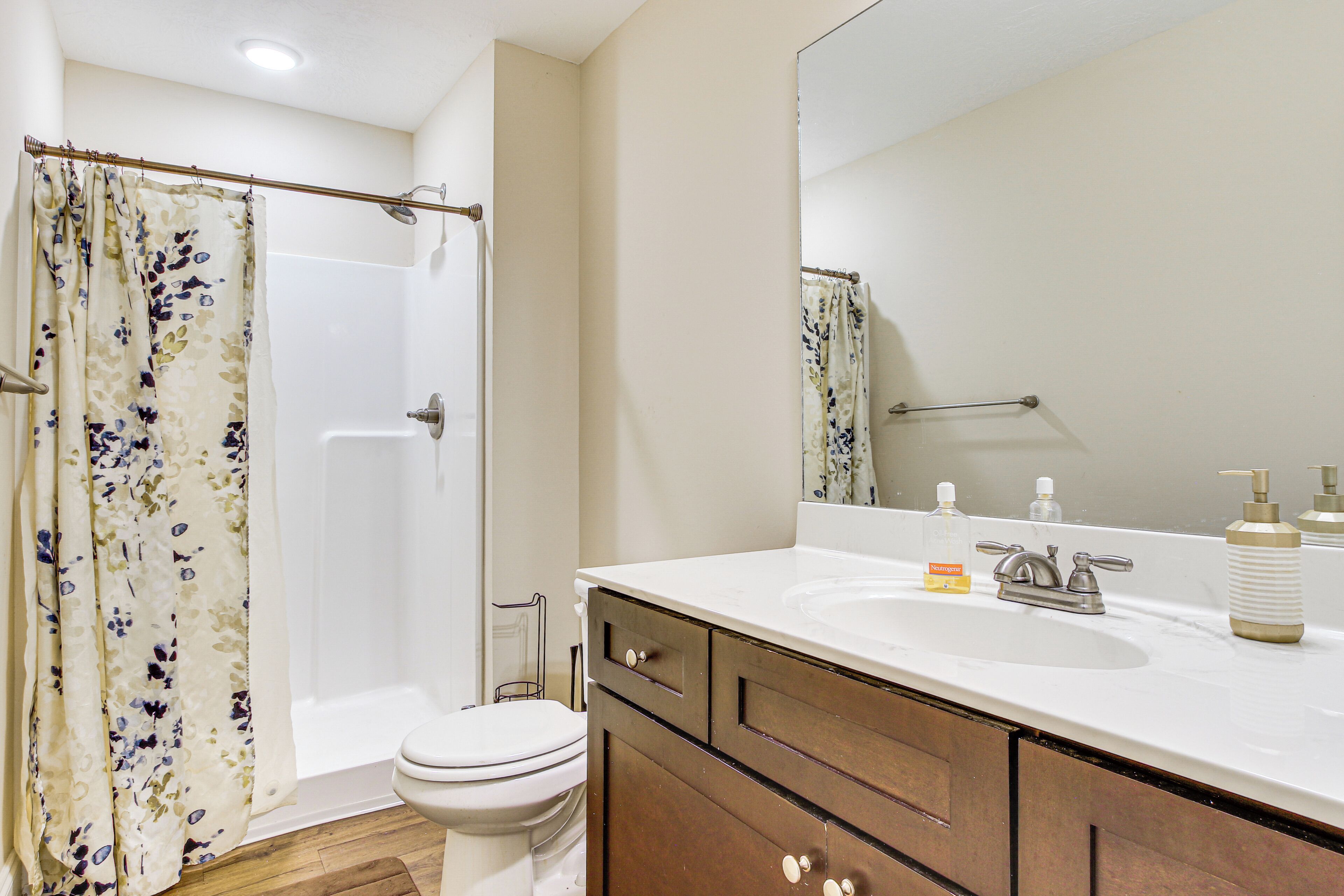 A bathroom with a shower curtain, toilet, sink, and wooden cabinets.