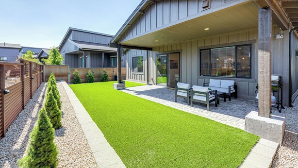 A modern house with a patio, outdoor seating, and a well-maintained lawn.