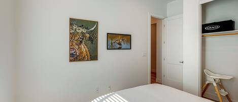Un dormitorio con una cama, un armario blanco y dos cuadros en la pared.