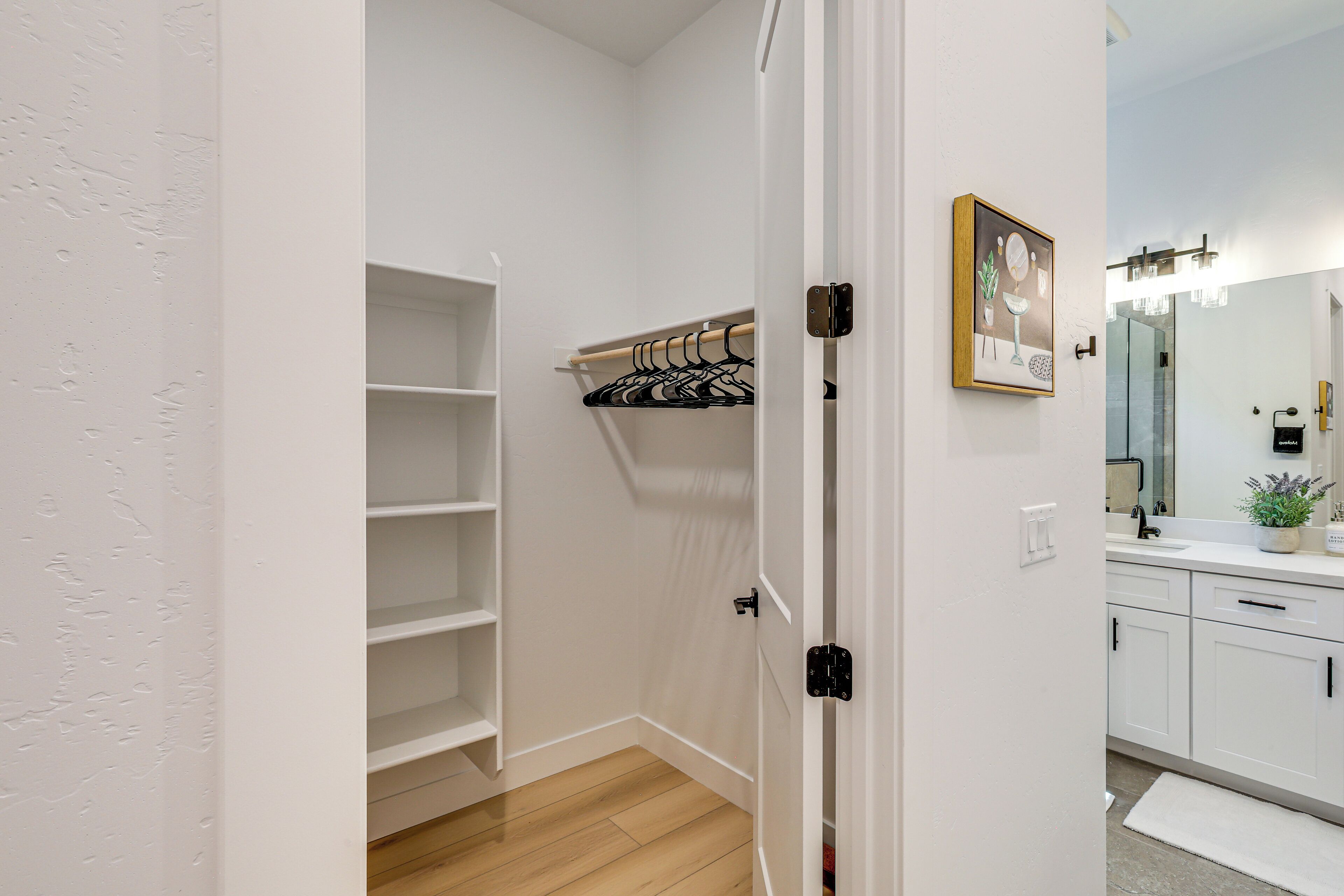 Une salle de bain moderne avec un lavabo blanc, un miroir et des armoires. Le sol est en bois et il y a un espace de douche blanc avec un porte-serviettes.