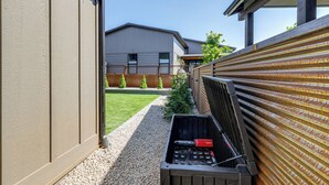 A narrow outdoor pathway leading to a building with a modern design, a wooden fence on one side, and a clear sky.
