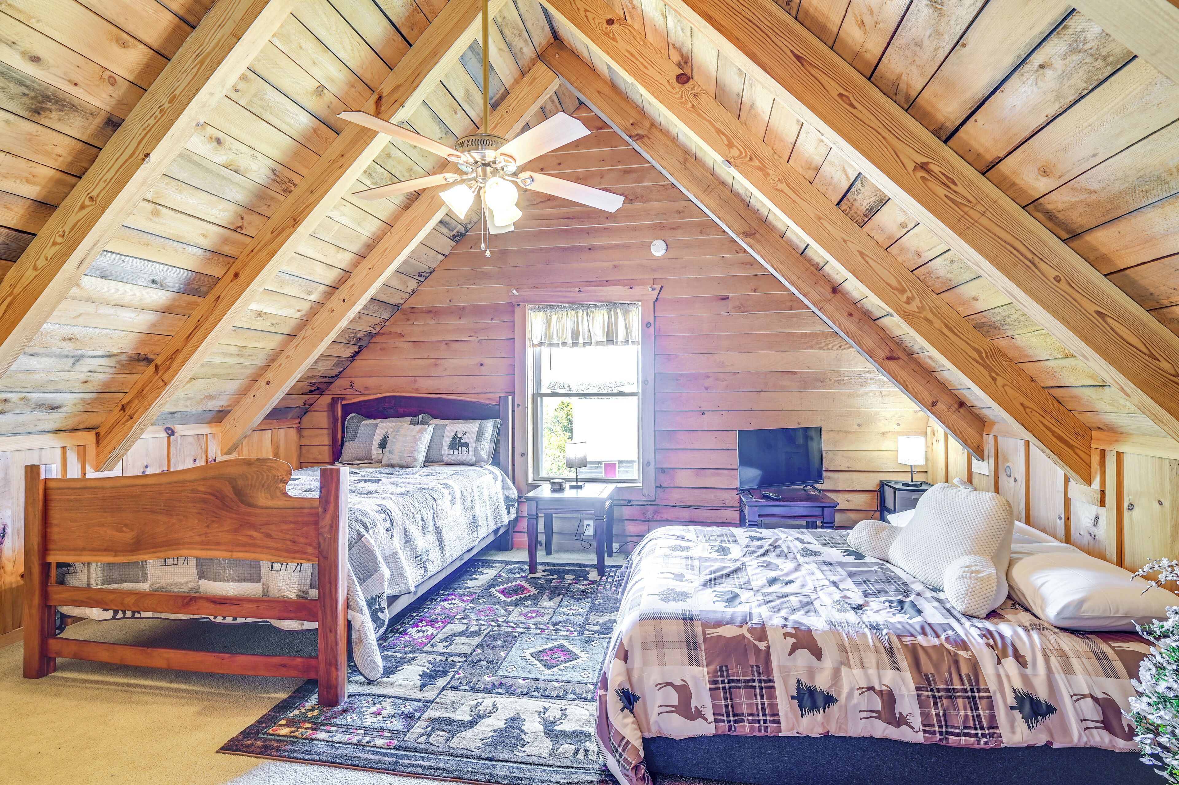 A cozy attic bedroom with two beds, a ceiling fan, and a window with curtains.