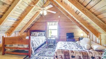 A cozy attic bedroom with two beds, a ceiling fan, and a window with curtains.