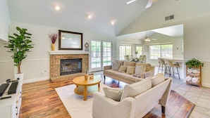 A spacious living room with a fireplace, a ceiling fan, and a dining area with bar stools. - Clovis Family Home: Private Pool, Near Old Town! (Clovis)