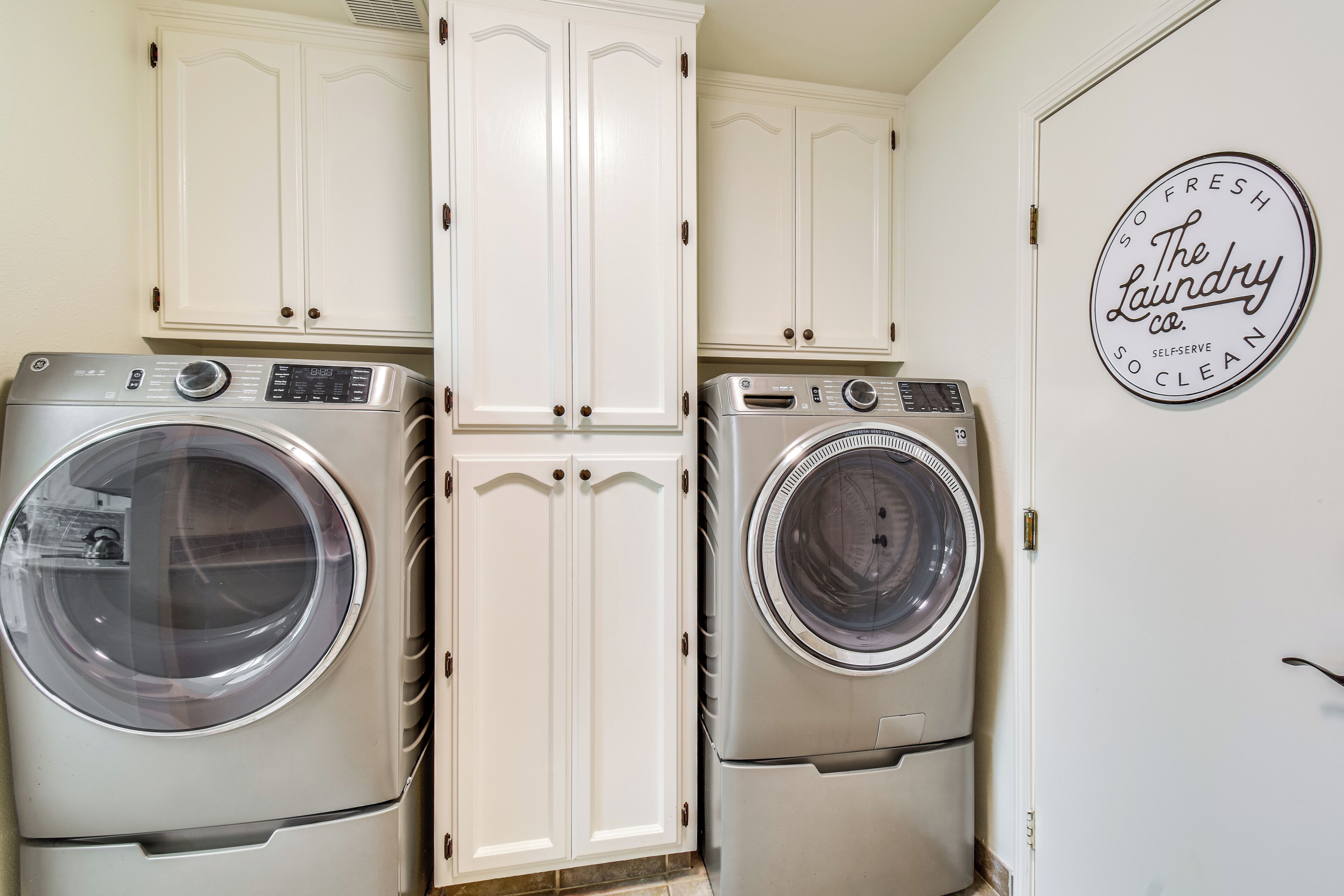 Une buanderie équipée de deux machines à laver à chargement frontal, de meubles blancs et d’une enseigne murale indiquant : « The Laundry Co. – laverie en libre-service, propreté garantie ».