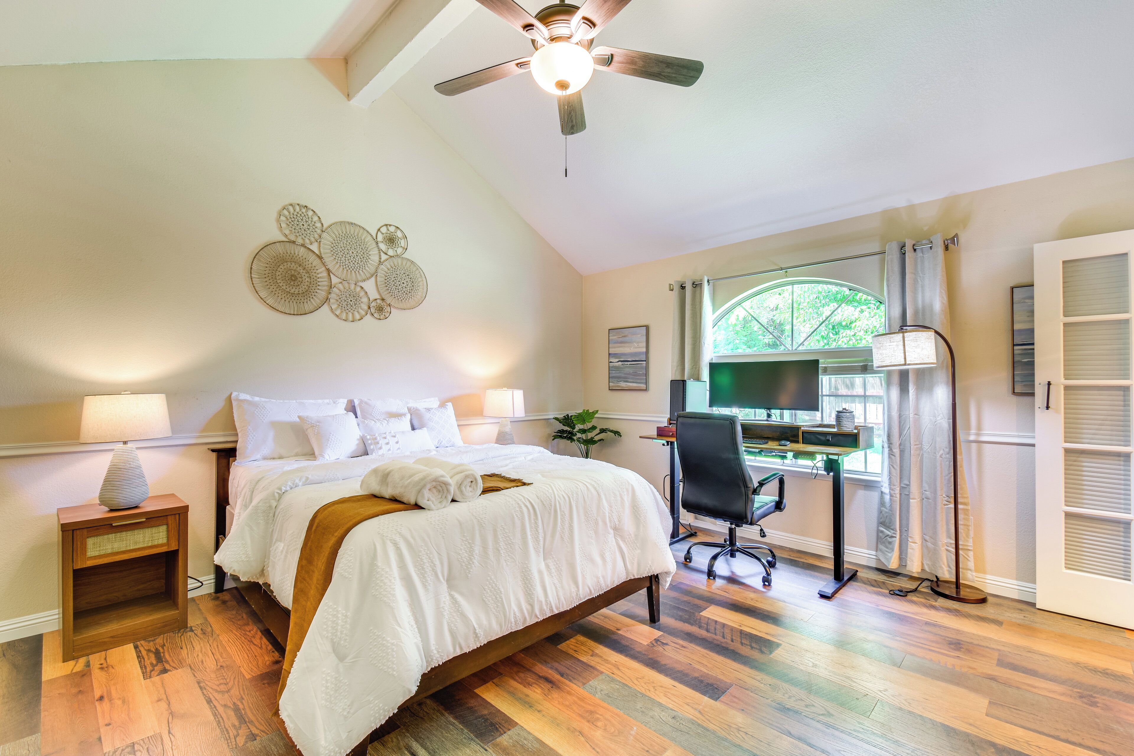 Une chambre à coucher comprenant un lit, un bureau, une chaise, un ventilateur de plafond et une fenêtre avec des rideaux.