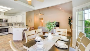 A modern kitchen with white cabinets, a dining area with a wooden table set for four, and a living area with a sofa and TV. - Clovis Family Home: Private Pool, Near Old Town! (Clovis)