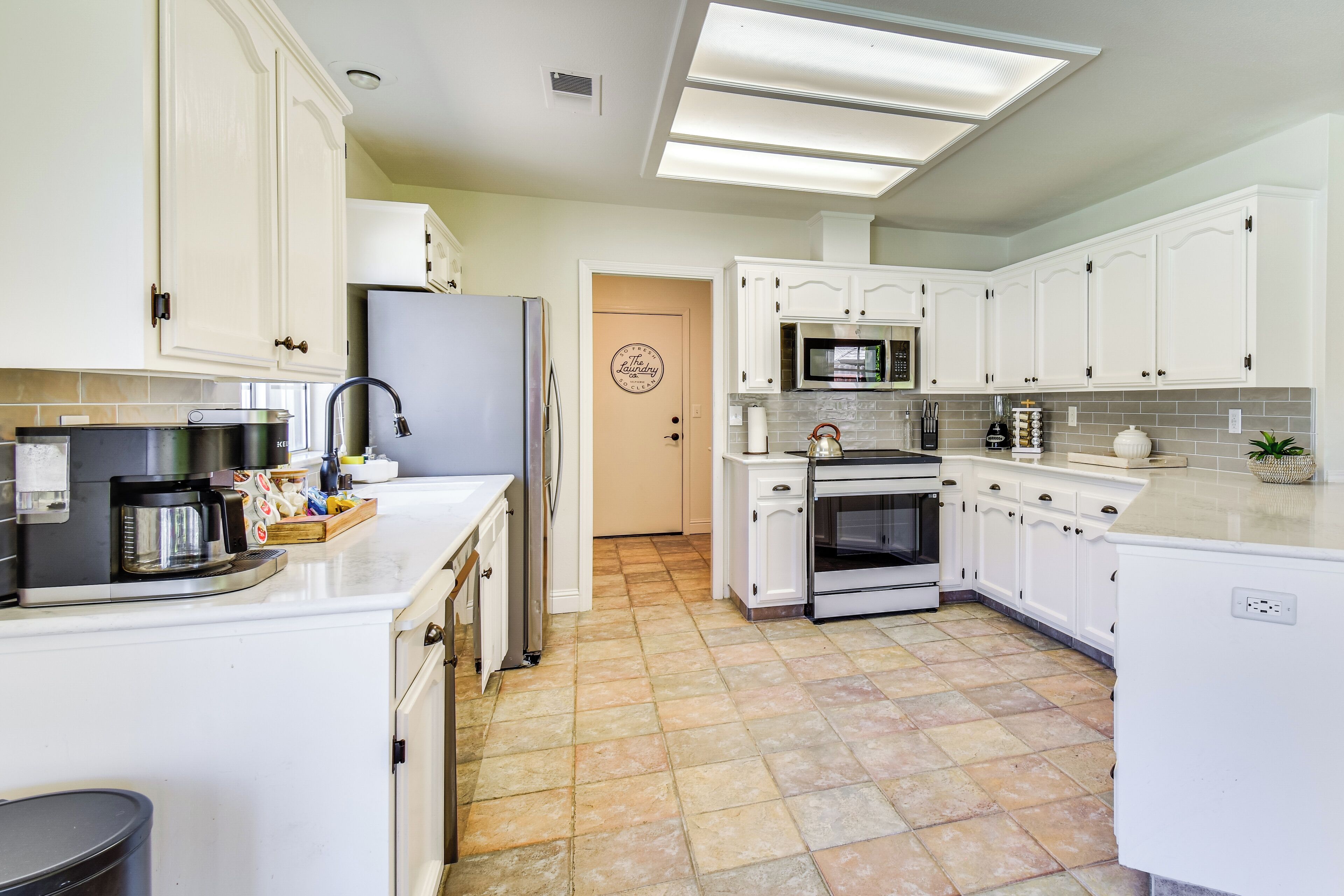 A modern kitchen with white cabinets, a refrigerator, a microwave, an oven, and a coffee maker.