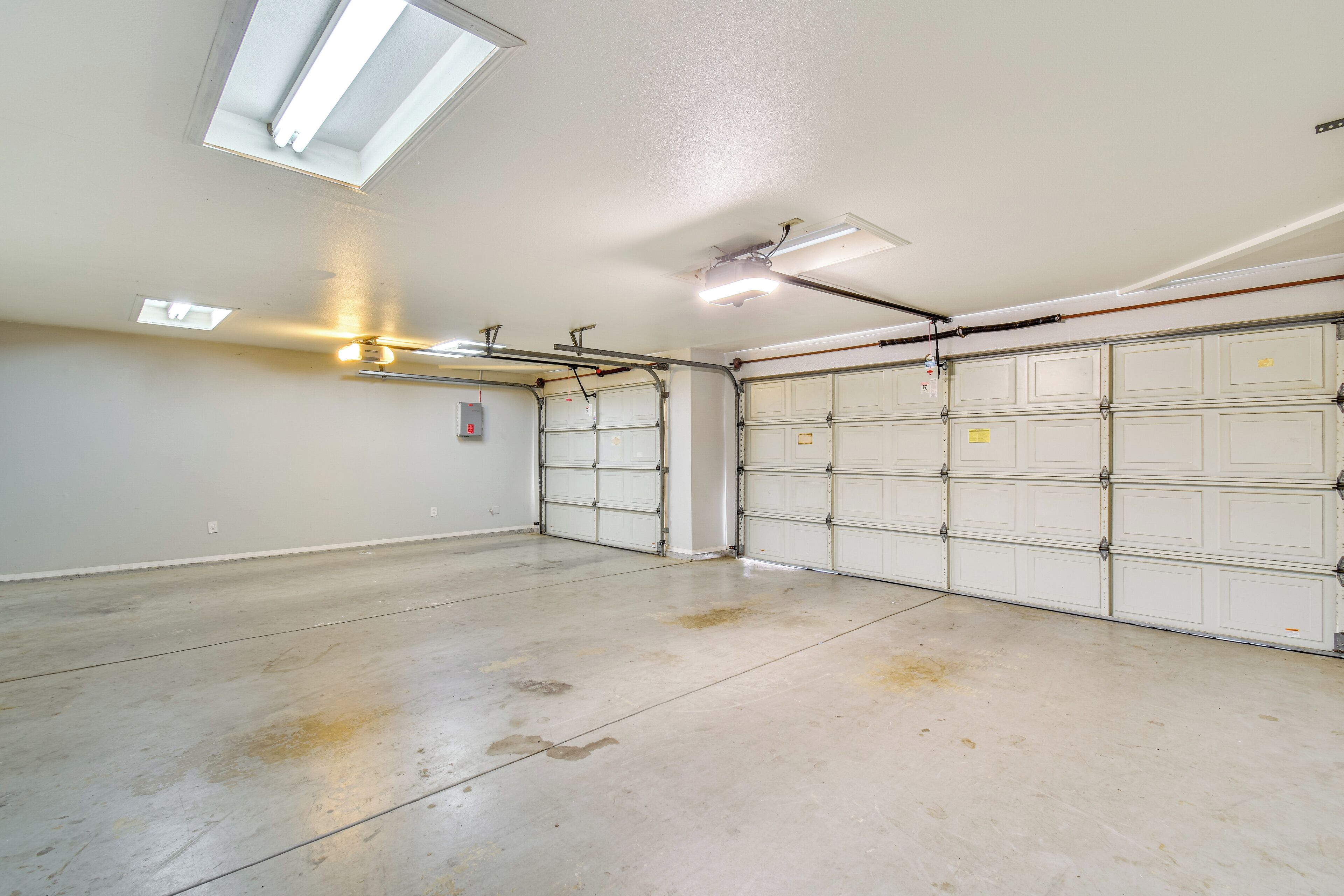 Ett rent, tomt garage med vita garagedörrar, takfönster och lysrörsbelysning.