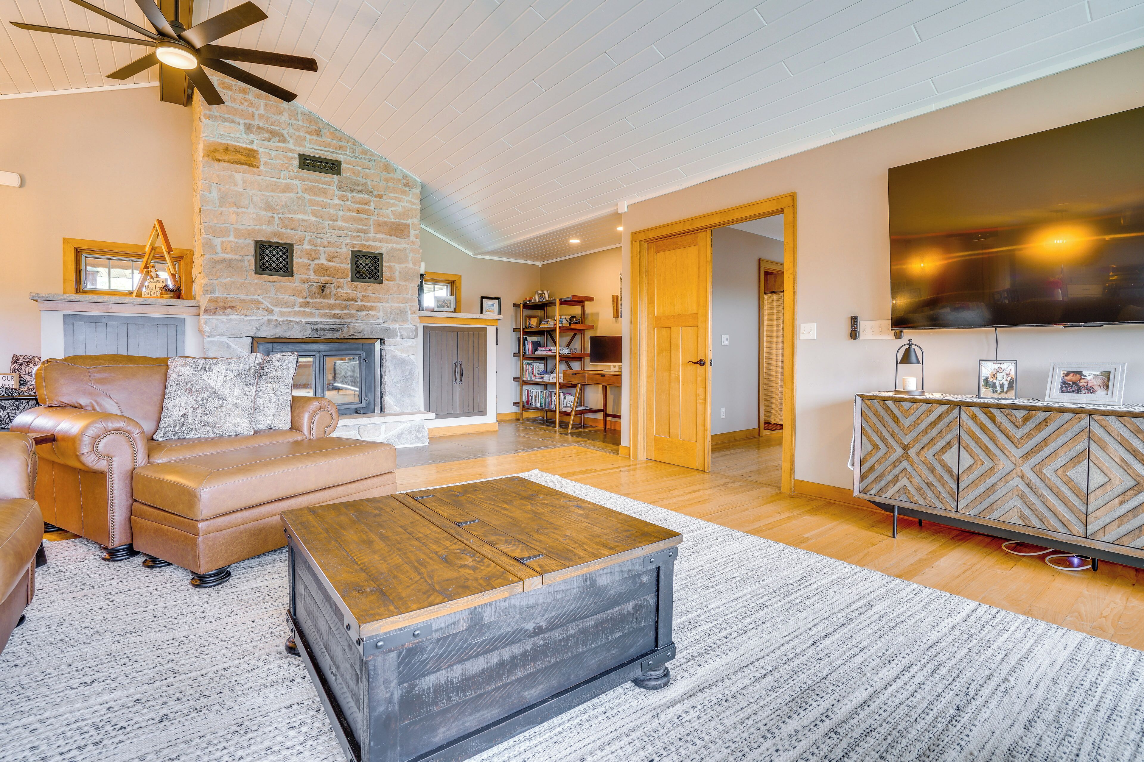 A spacious living room with a stone fireplace, leather sofa, and a large TV.