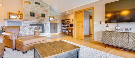 A spacious living room with a stone fireplace, leather sofa, and a large TV.