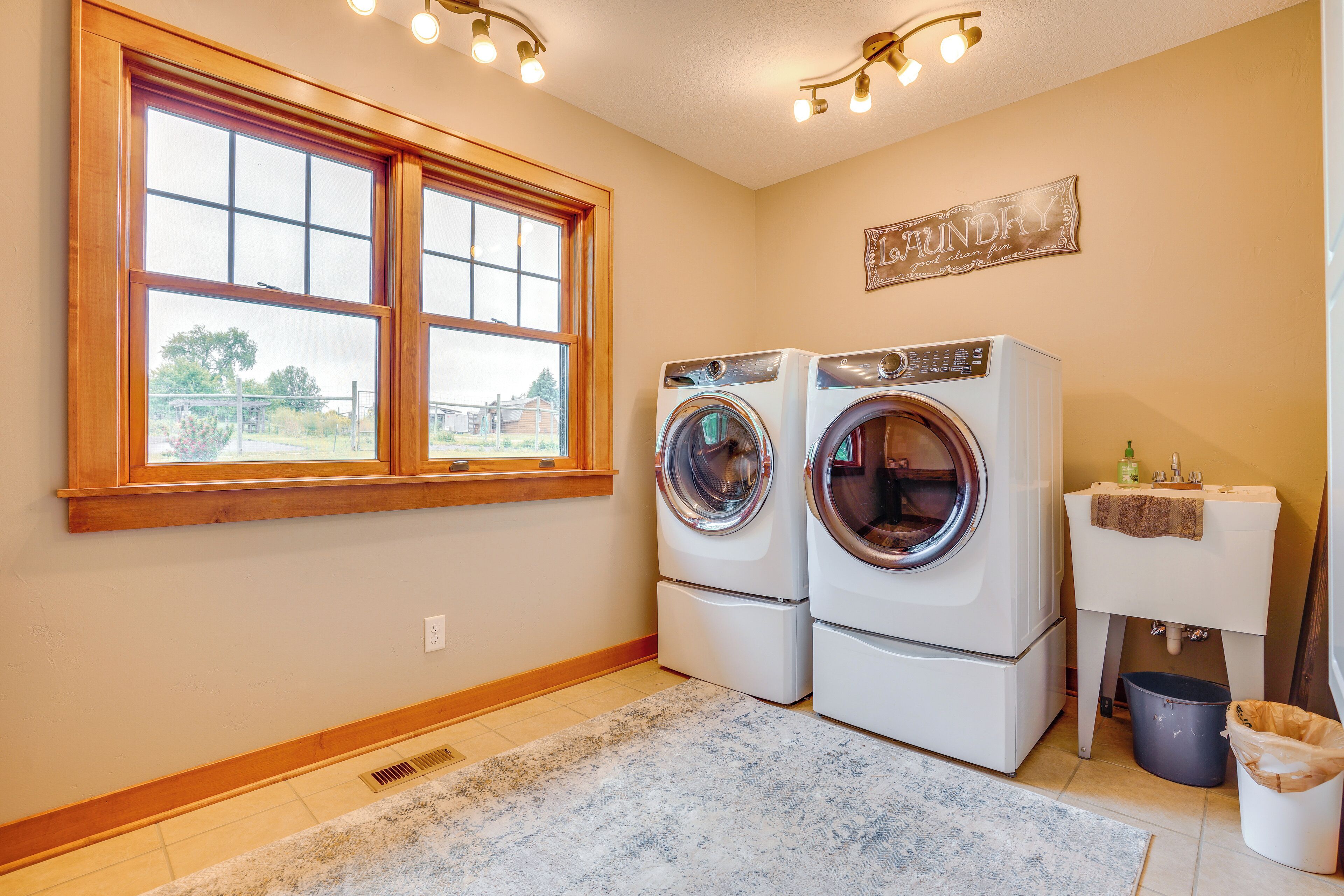 A laundry room with two front-loading washers and dryers, a window with a view of the outside, and a wall-mounted sign that reads "Laundry".