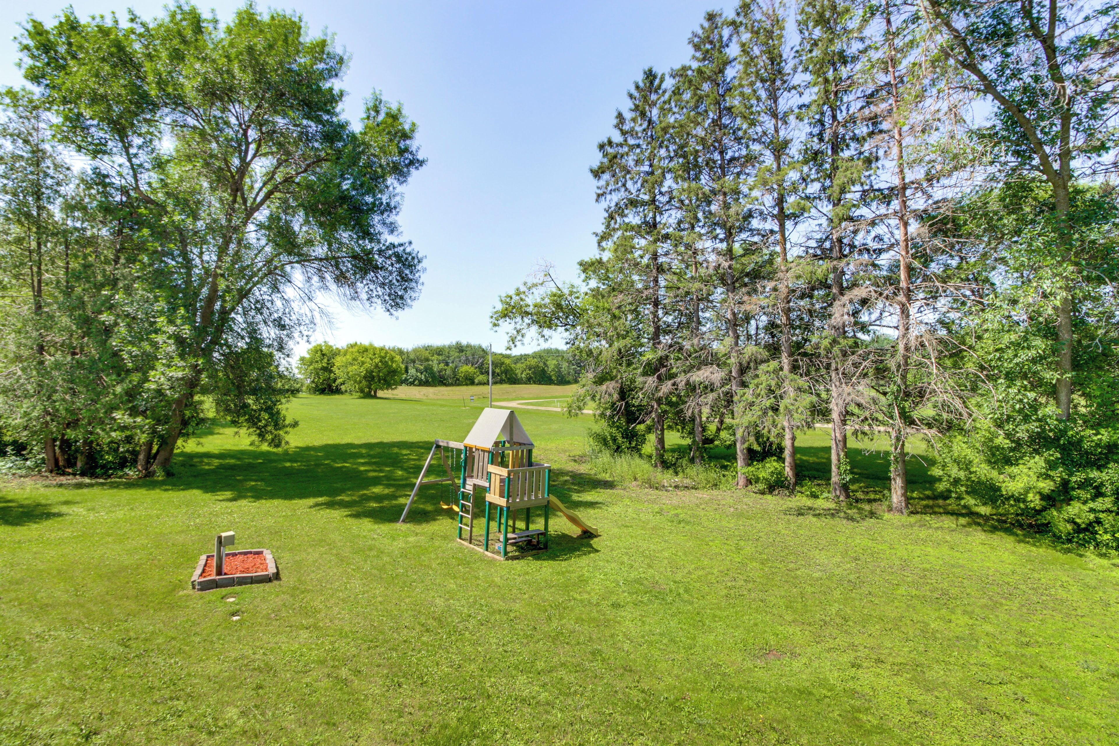 A playground with a climbing structure and a slide, surrounded by trees and grass.