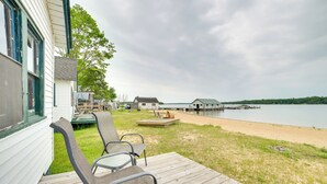A wooden deck with chairs, a view of a lake, and a dock in the background. - Complimentary Boat Rentals! Lake Huron Cabin (Cedarville)