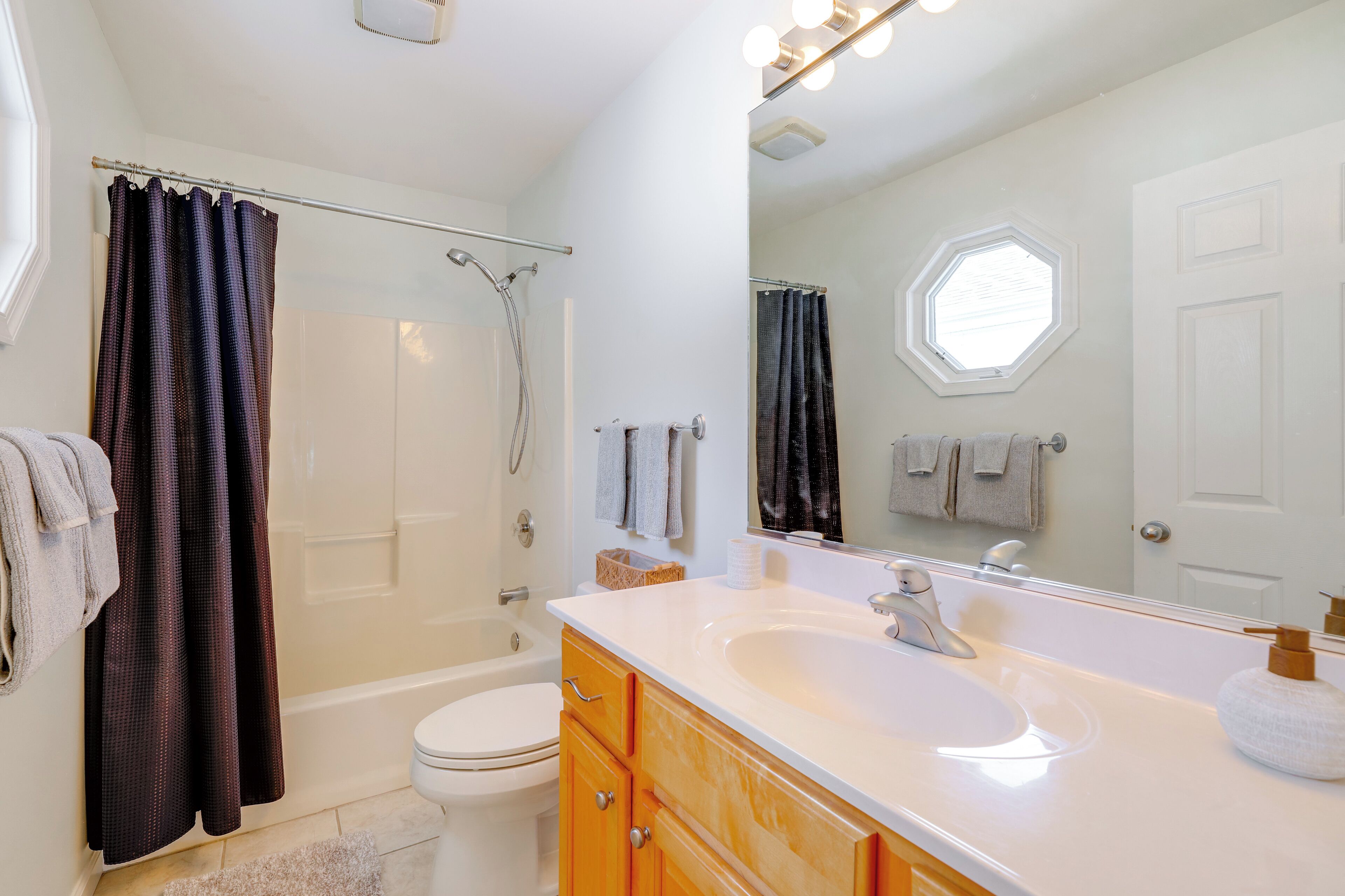 A modern bathroom with a bathtub, toilet, and vanity with a large mirror.