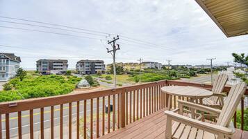 A wooden deck with a table and chairs, overlooking a road with buildings and greenery.