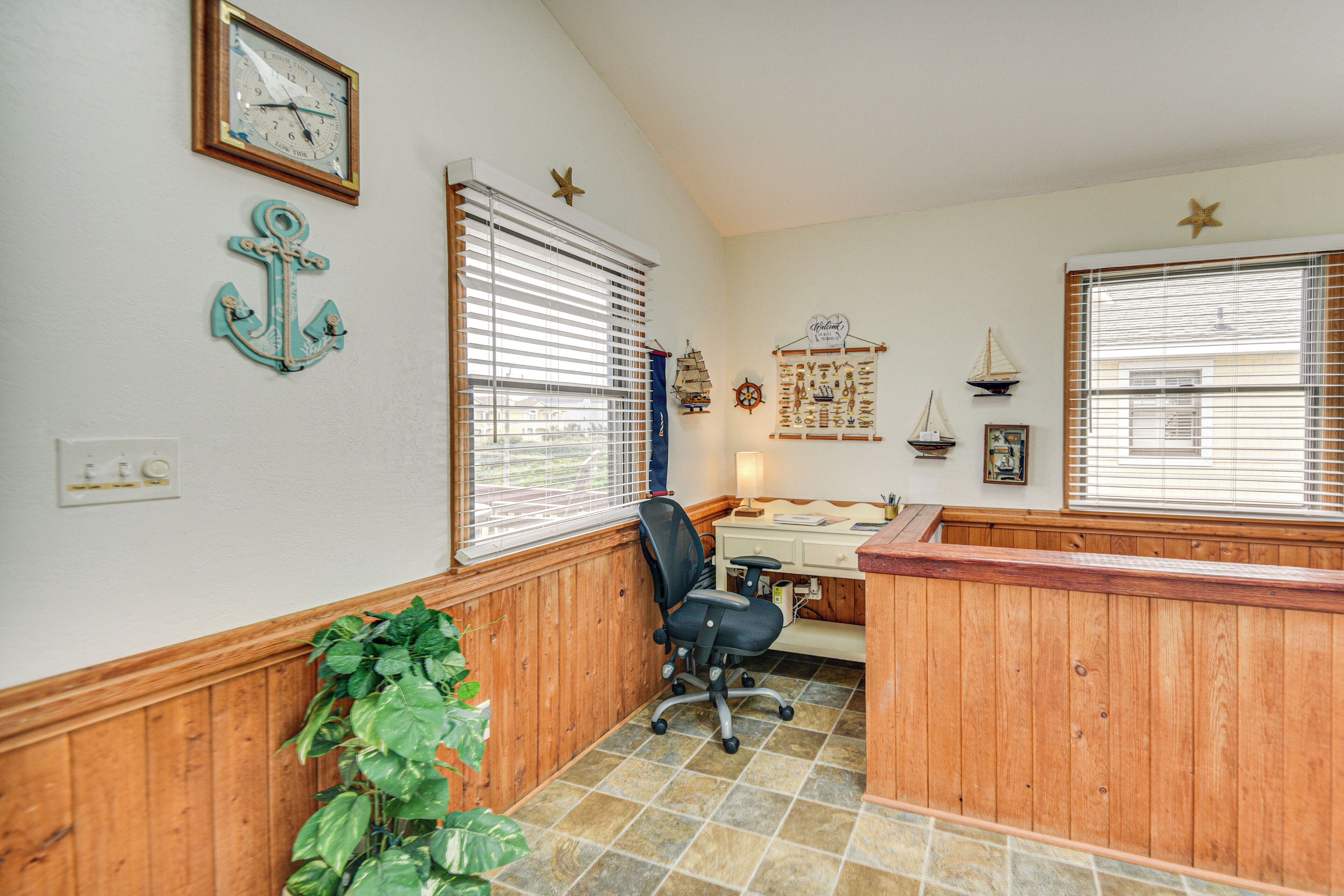 A room with wooden paneling, a desk with a chair, a potted plant, and nautical decor including an anchor and a ship.