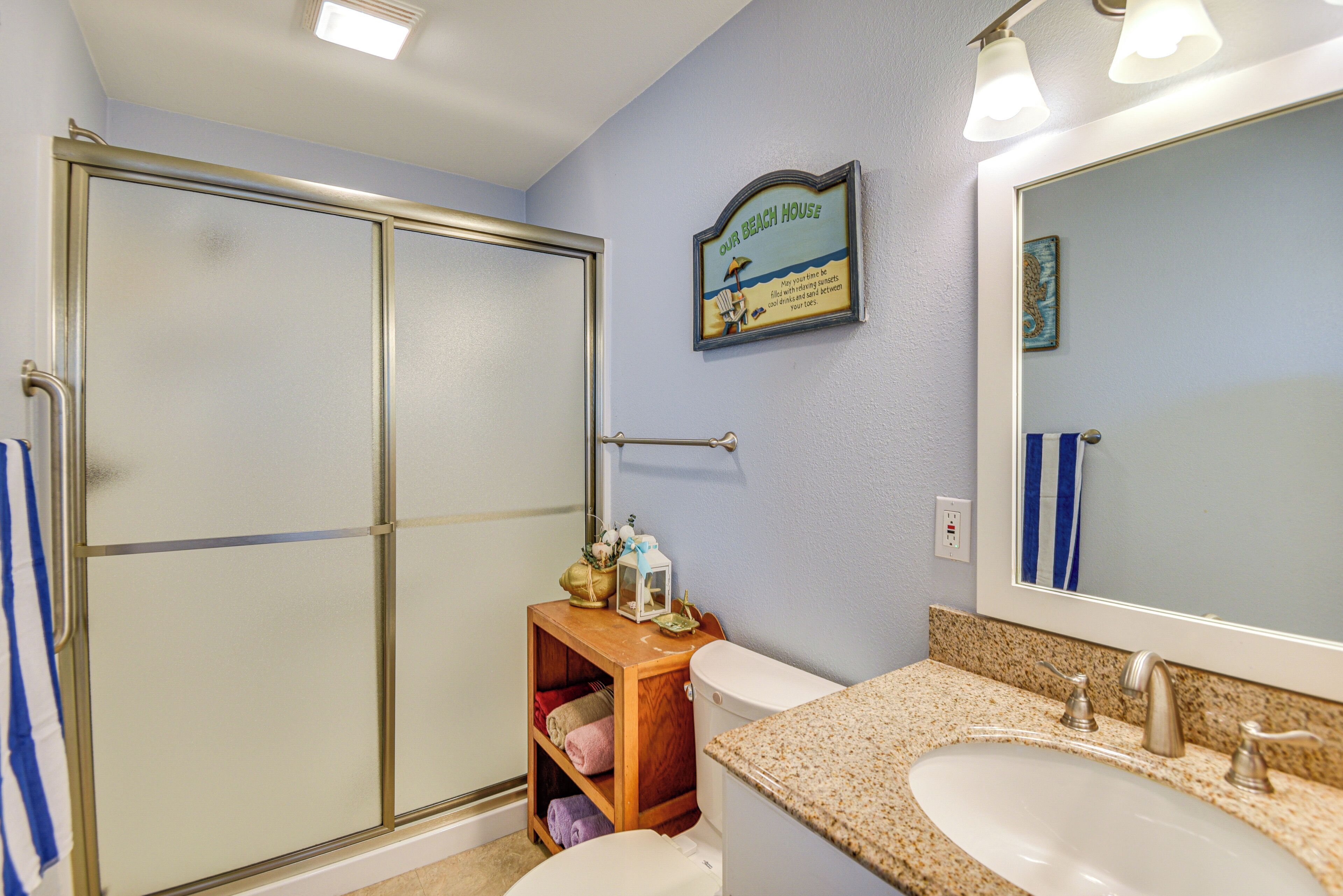 Une salle de bain avec une douche à parois de verre, une étagère en bois avec des serviettes, des toilettes et un lavabo avec un miroir.