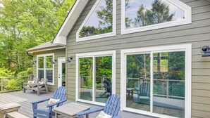A deck with two Adirondack chairs and a table, large windows, and a view of a deck and trees. - 11 Mi to State Park: Home w/ Dock in Mill Spring! (Mill Spring)