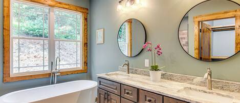 A bathroom with a freestanding bathtub, a double sink vanity, and two wall-mounted mirrors.
