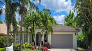 A single-story house with a garage, surrounded by lush greenery and palm trees. - Naples Escape w/ Private Pool 5 Mi to Beach (Naples)