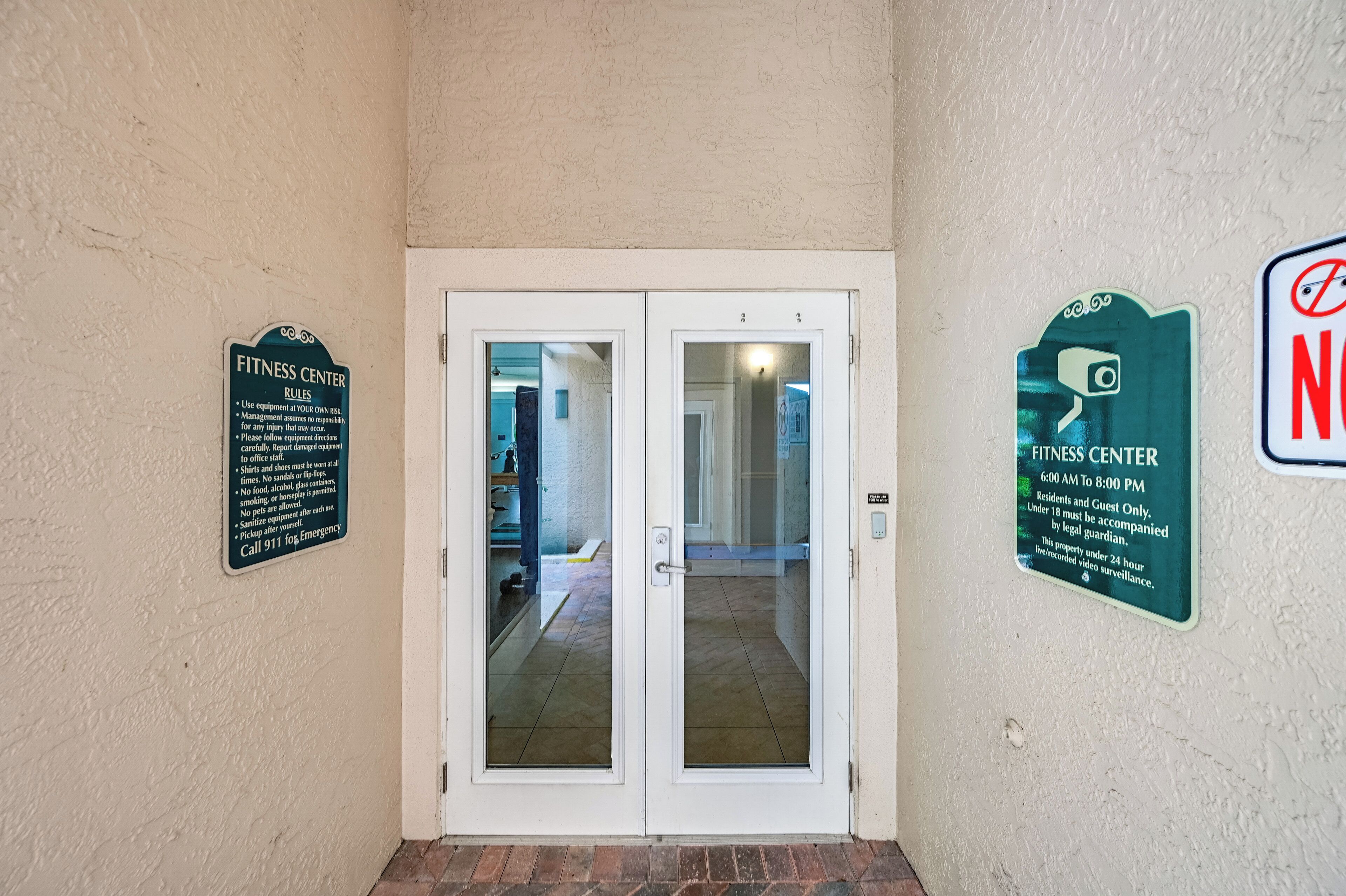 A fitness center entrance with glass doors, a sign listing rules, and a surveillance sign.