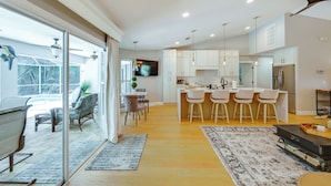 A modern kitchen with white cabinets, a central island with bar stools, and a dining area with a table and chairs. - Naples Escape w/ Private Pool 5 Mi to Beach (Naples)