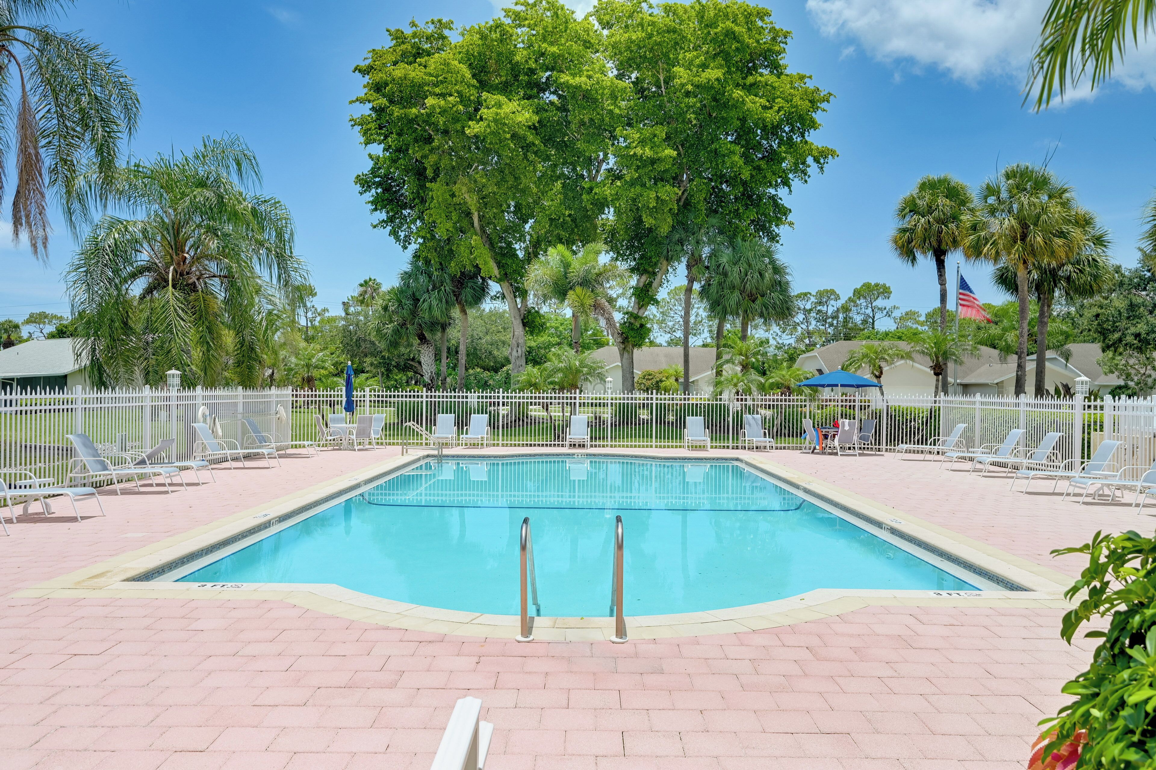 Una piscina rectangular con cerca blanca y sillas de descanso alrededor.