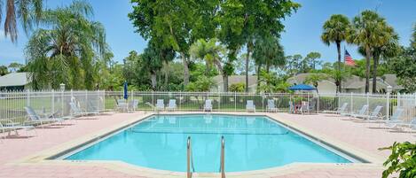 Una piscina rectangular con cerca blanca y sillas de descanso alrededor.